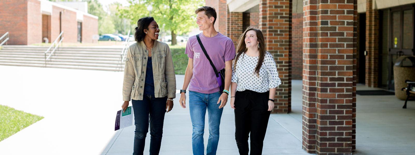 three students walking on sidewalk on campus